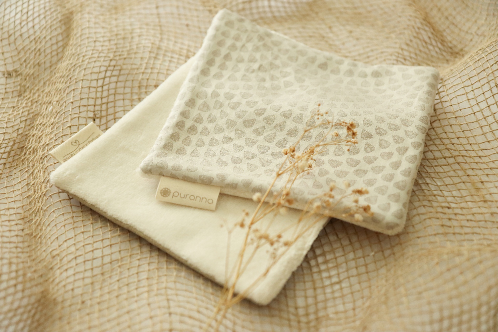 Duas bolsas pequenas em tecido creme e bege com padrão de corações, sobre tecido bege quadriculado com flores secas