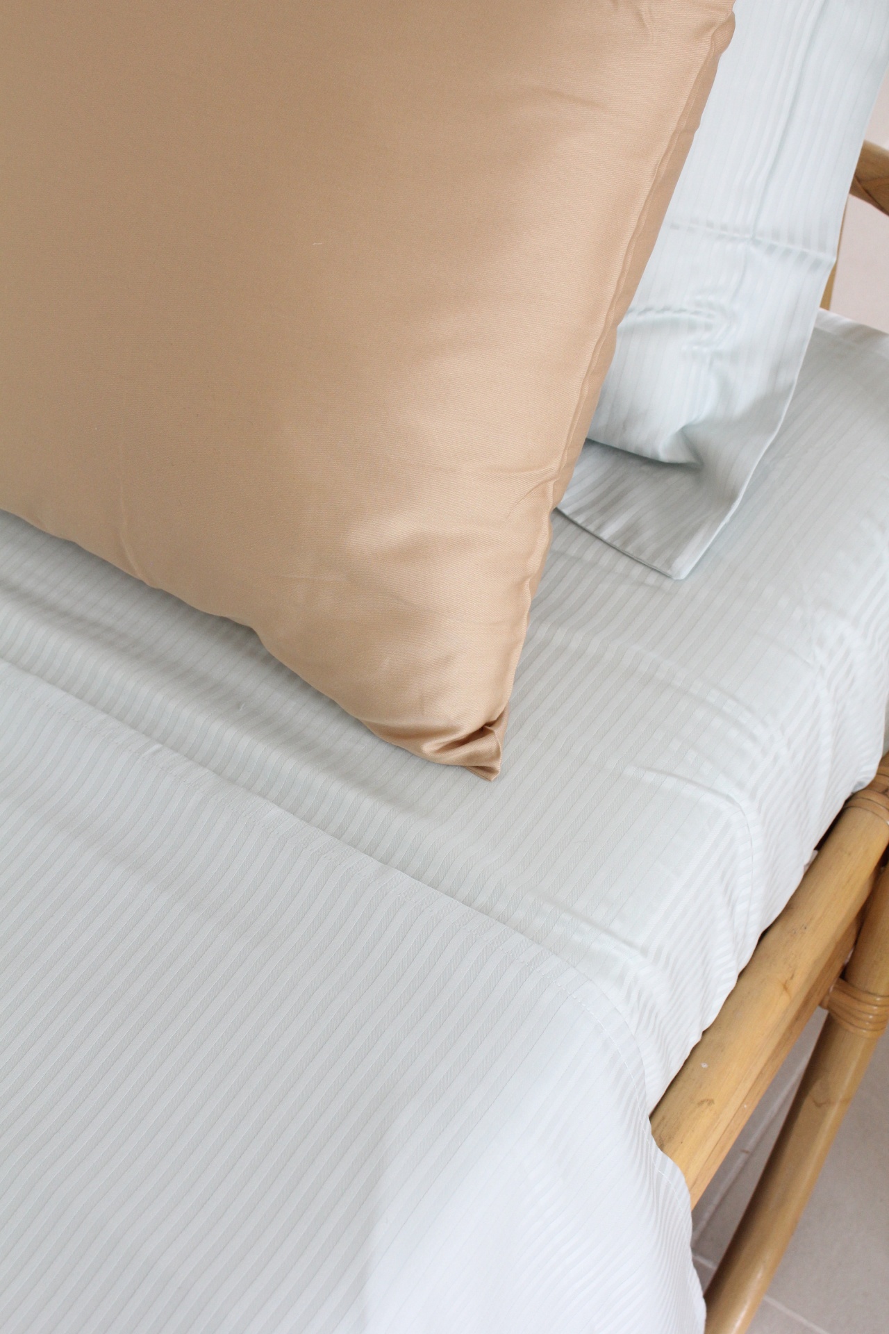 Cama com roupa de cama branca de riscas finas e almofada castanha