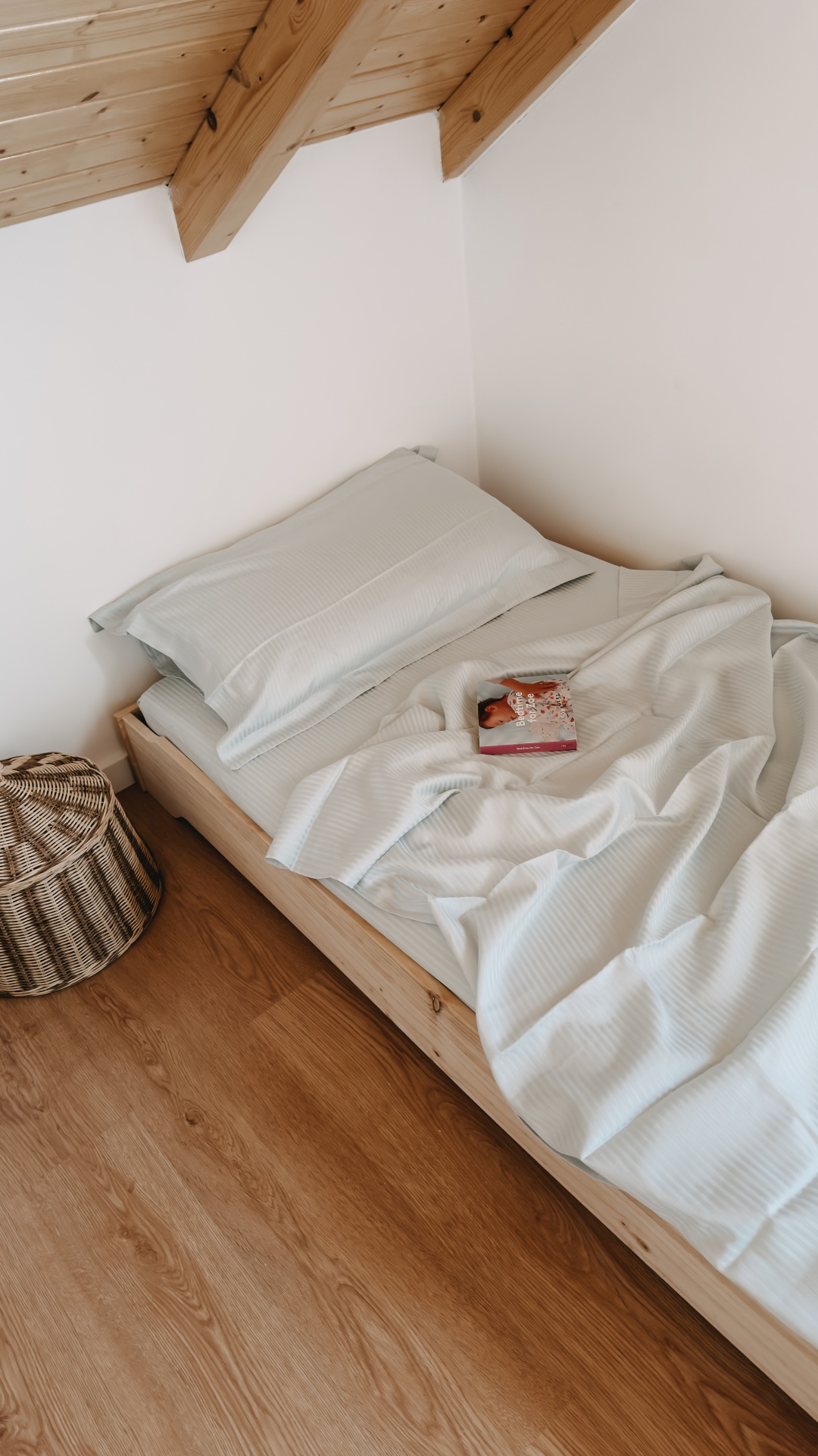 Cama de madeira com roupa de cama azul-claro e cesto de verga no chão