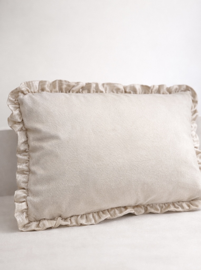 Almofada bege claro com borda franzida sobre superfície semelhante