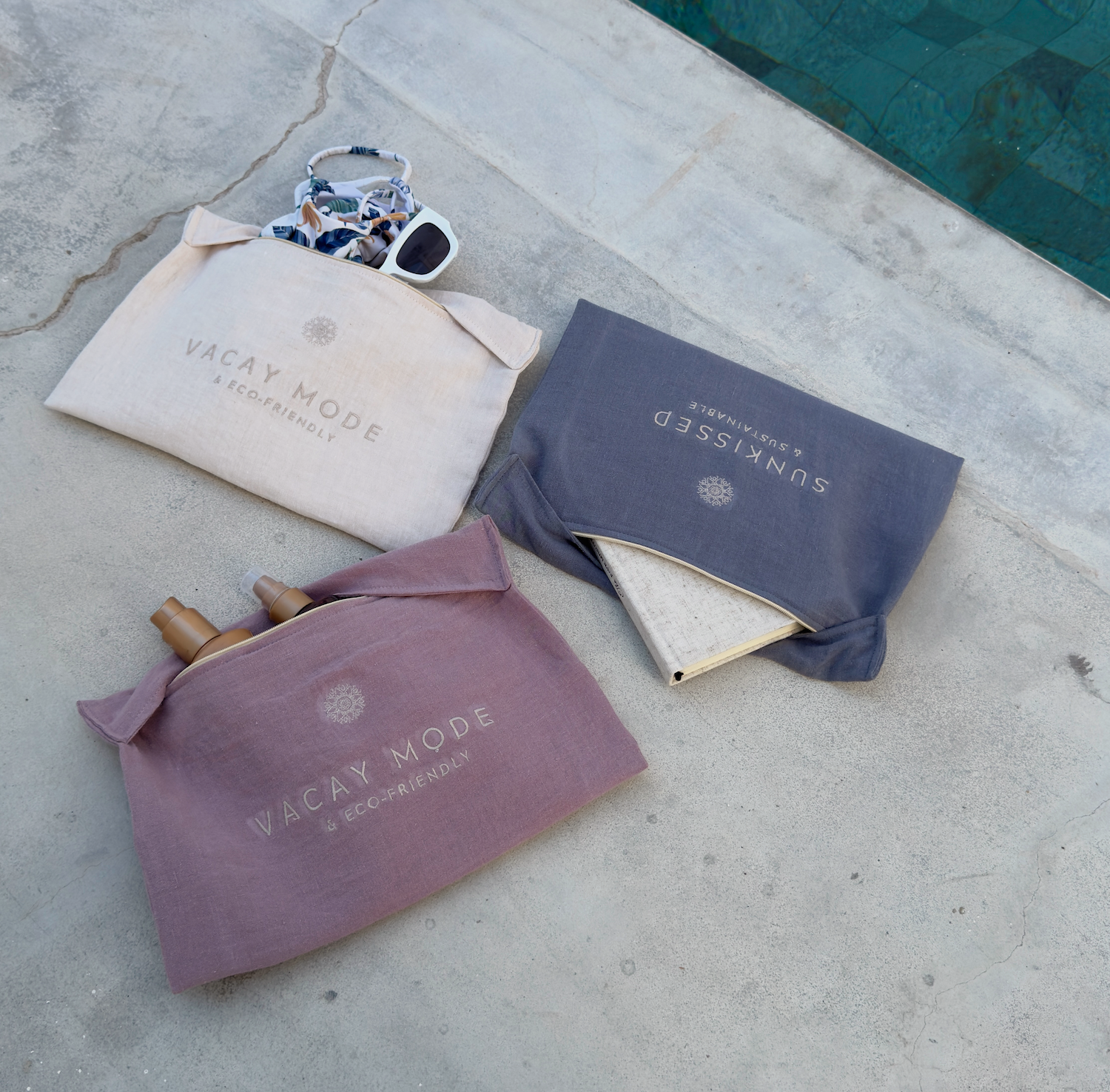 Três sacos de tecido com fecho e textos VACAY MODE e SUNKISSED sobre cimento junto a piscina
