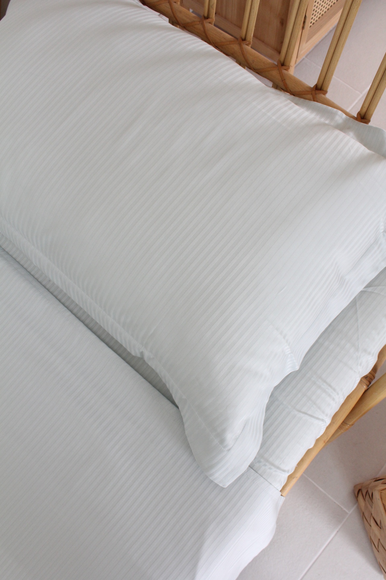 Almofada e edredão brancos com padrão riscado num ambiente com mobiliário de madeira clara