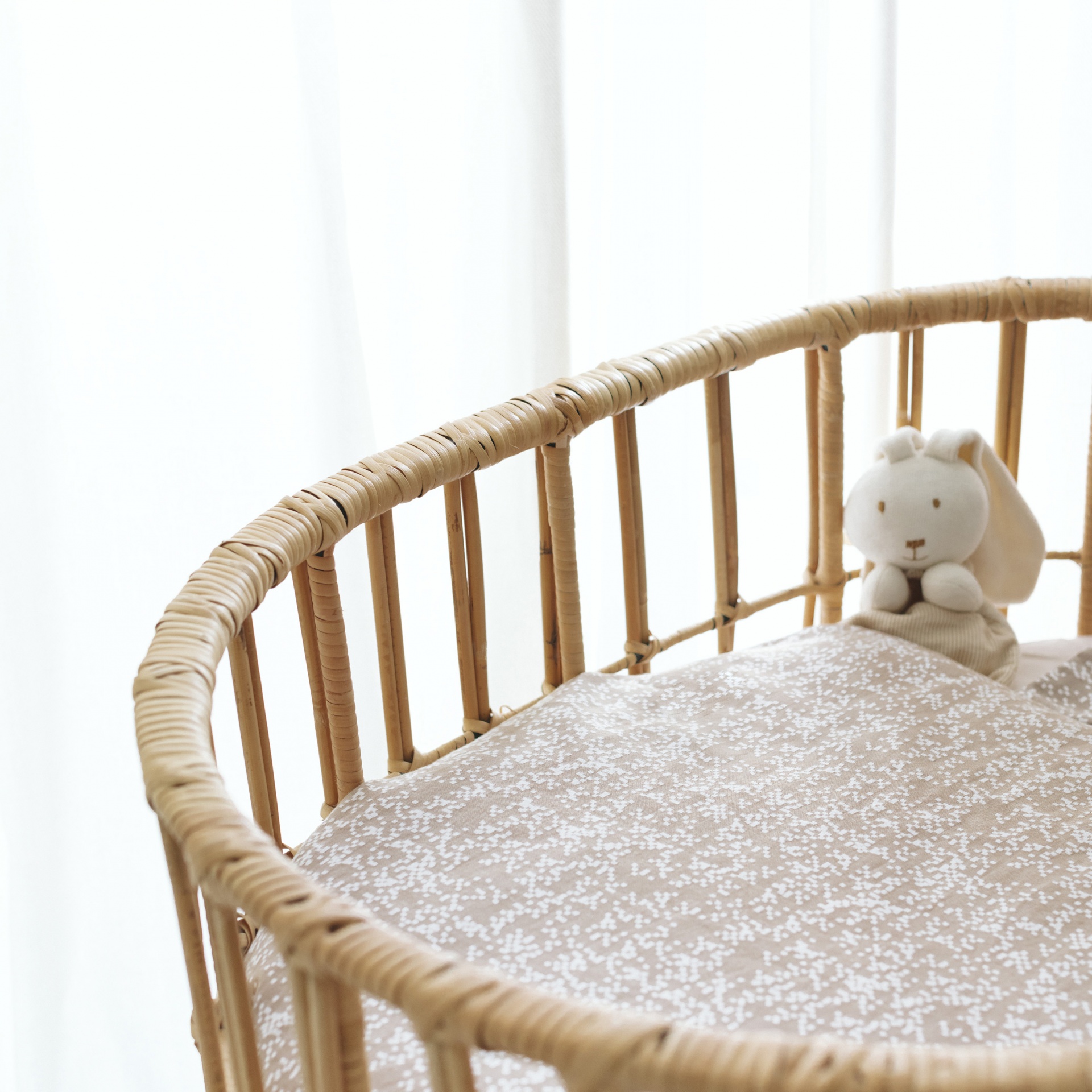 Berço redondo de vime com colchão estampado e peluche creme.