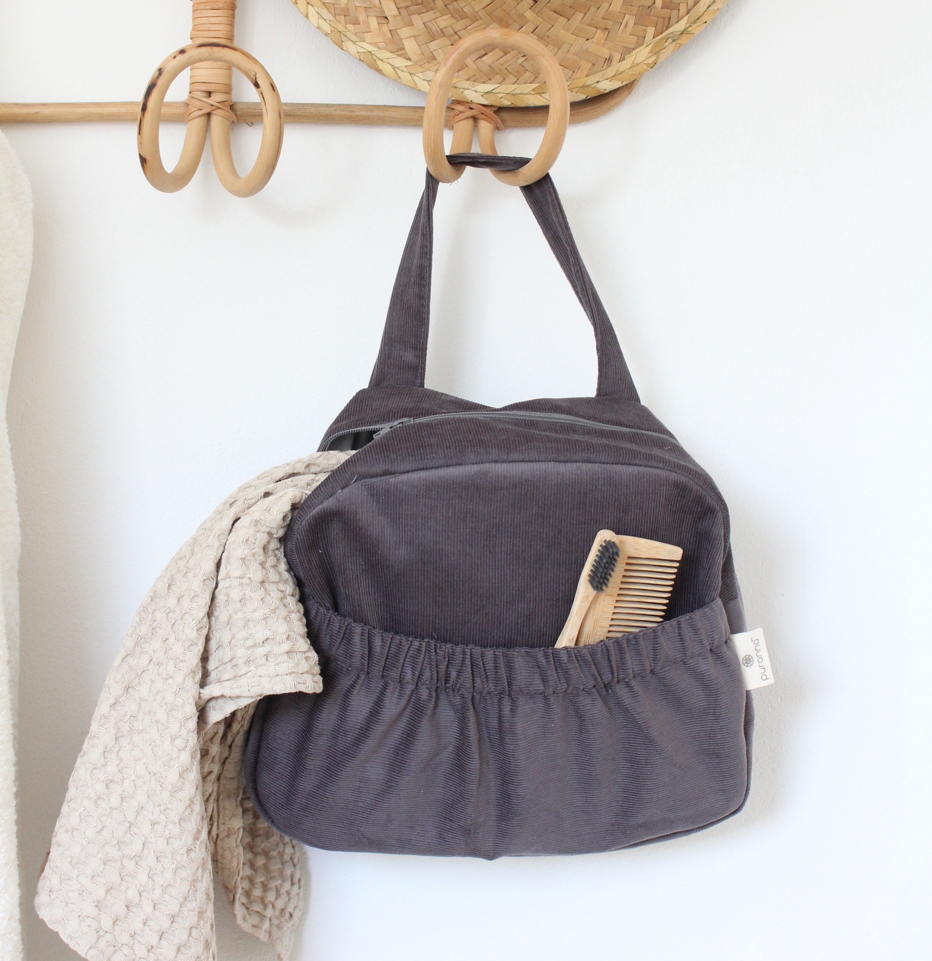 Bolsa cinzenta com bolso frontal elástico pendurada com pano bege e utensílios de madeira