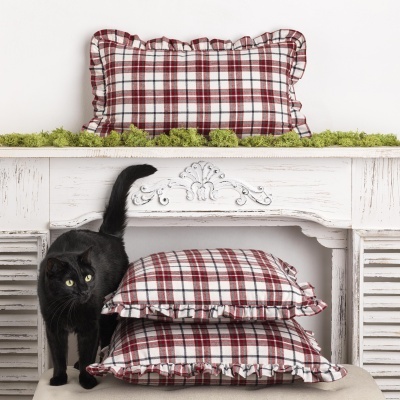 Almofadas xadrez vermelhas e brancas com bordas onduladas junto a mesa branca entalhada e gato preto