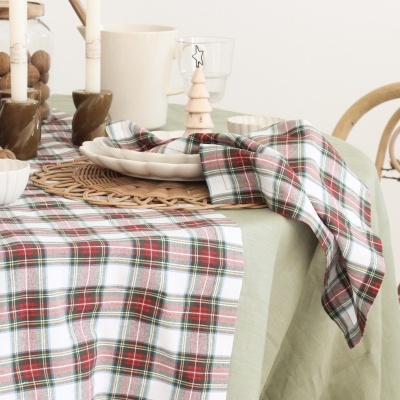 Mesa com toalha verde, caminho de mesa e guardanapo xadrez, pratos brancos, castiçais, copo e decoração em madeira