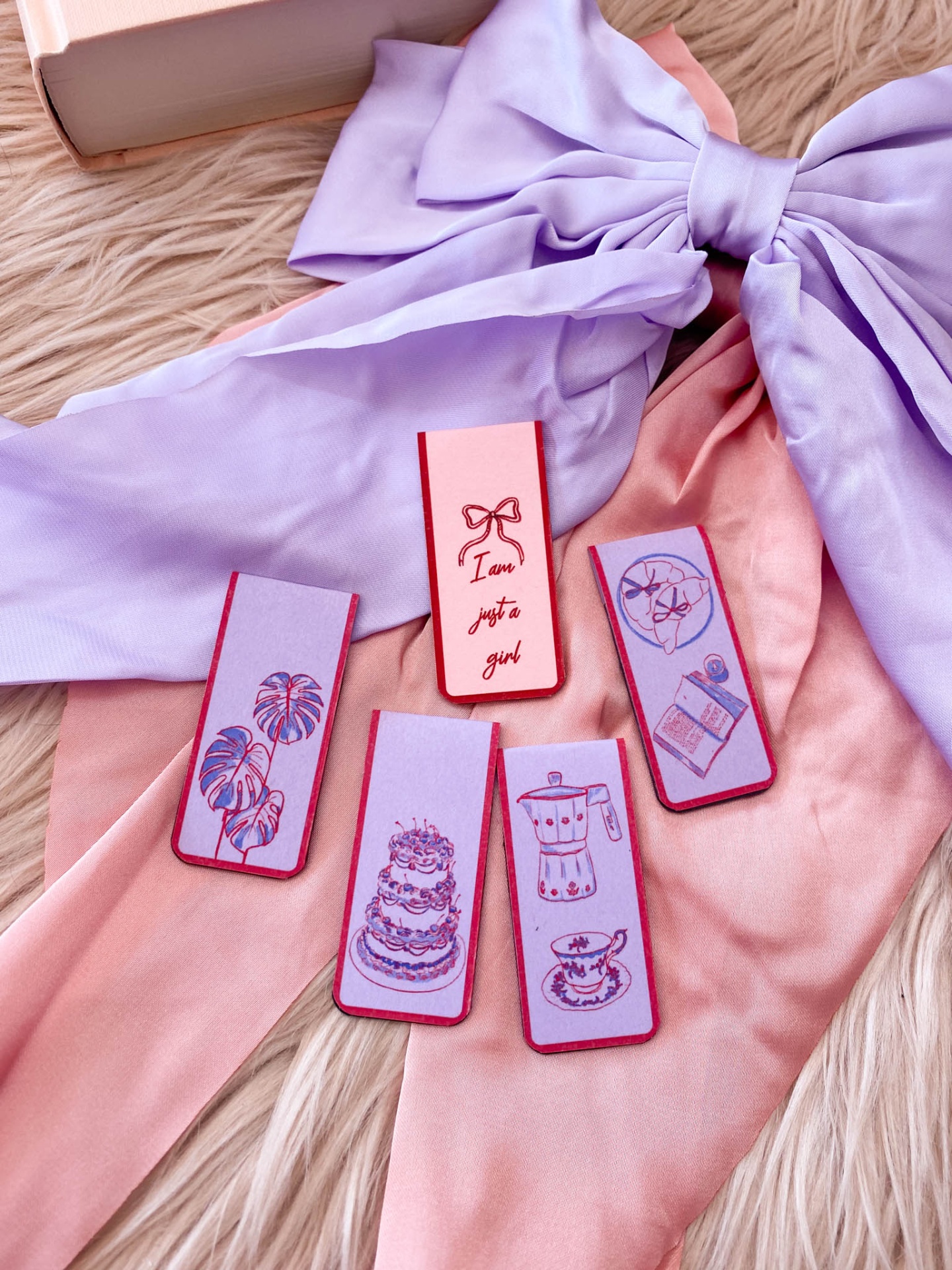 Cinco marcadores de livro decorados em tecido lilás e rosa sobre tecido com laço lilás e fundo felpudo bege