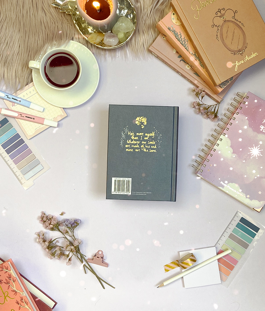 Mesa com cadernos, chávena com chá, paletas de cores, flores secas e vela acesa.