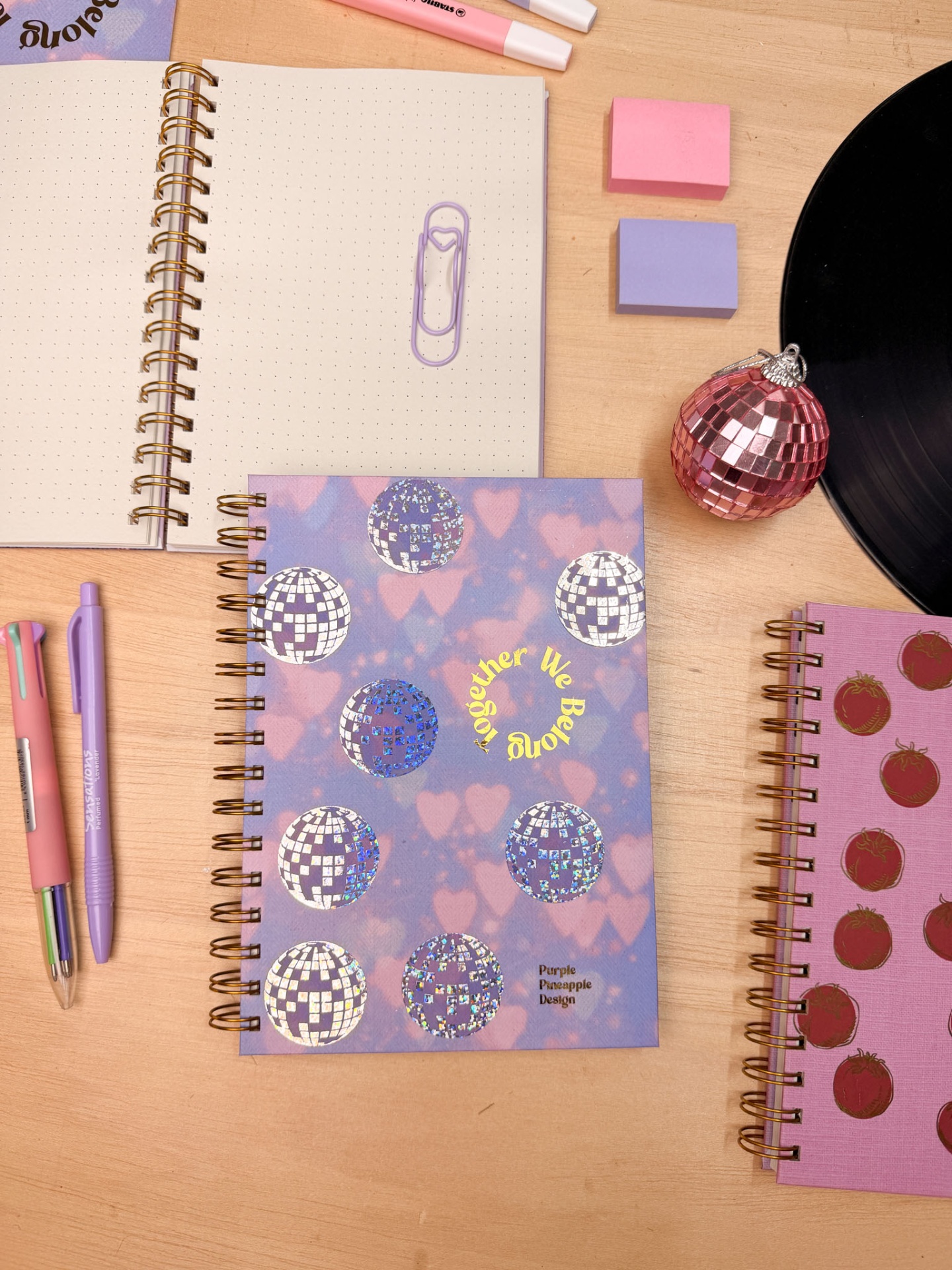 Três cadernos espirais com capas decorativas e um aberto com página pontilhada sobre mesa de madeira.