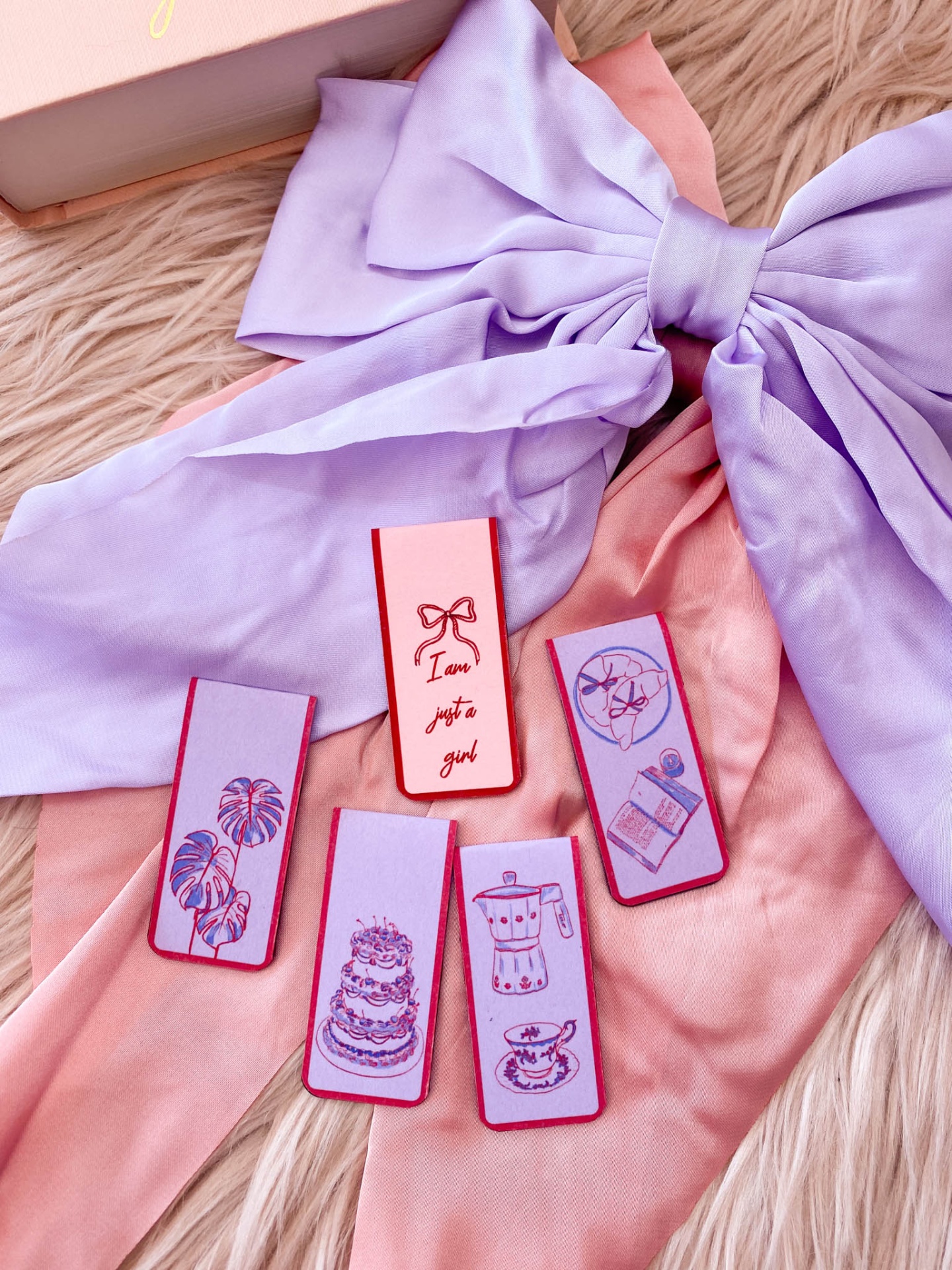 Marcadores de página coloridos com ilustrações e texto sobre tecido lilás e cor-de-rosa