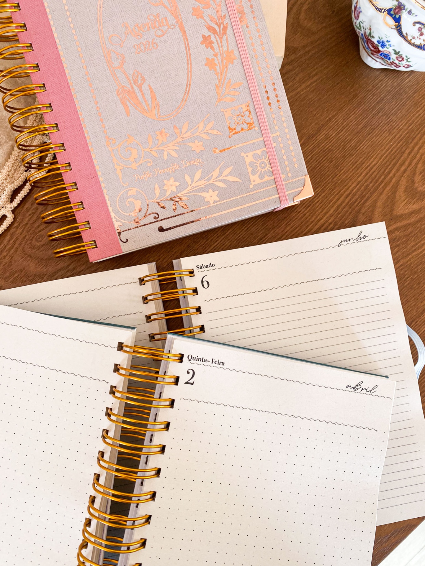 Agenda 2026 rosa com detalhes dourados e páginas internas com datas em português sobre mesa de madeira