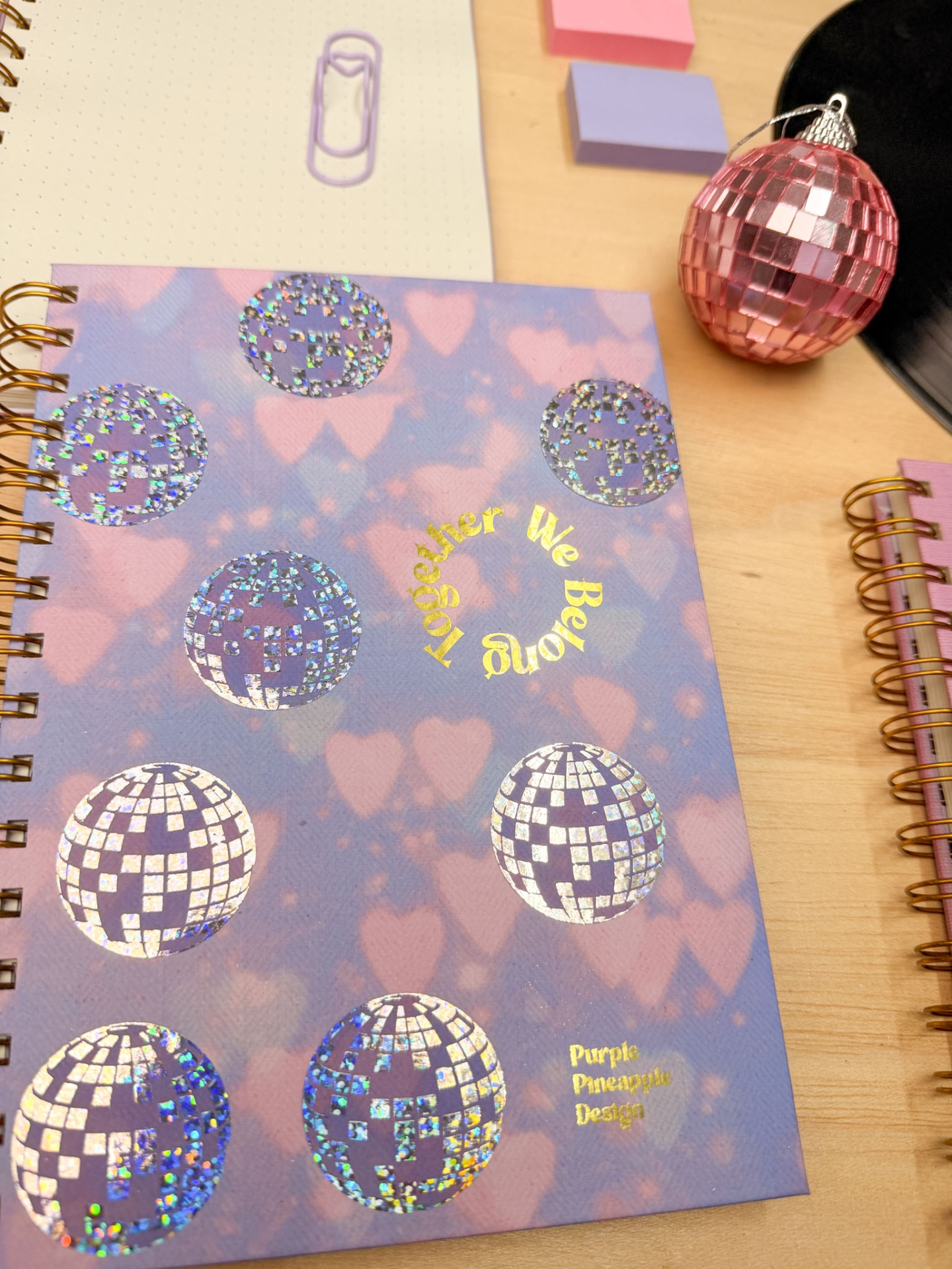 Caderno azul e rosa com decoração holográfica e texto dourado em mesa de madeira