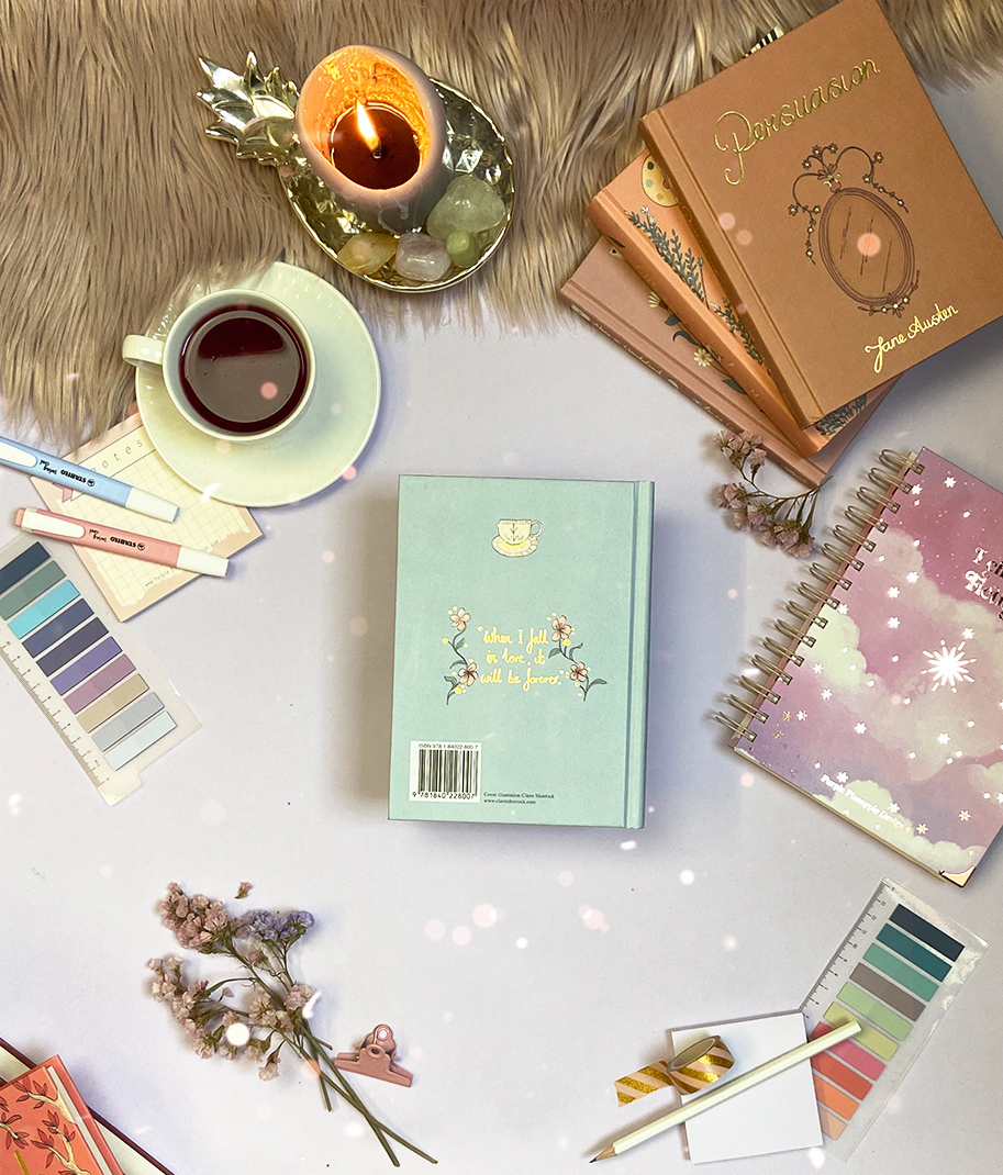 Conjunto de livros e cadernos coloridos, chá em xícara branca, paletas de cores, flores secas e vela acesa sobre mesa clara com textura de pele sintética