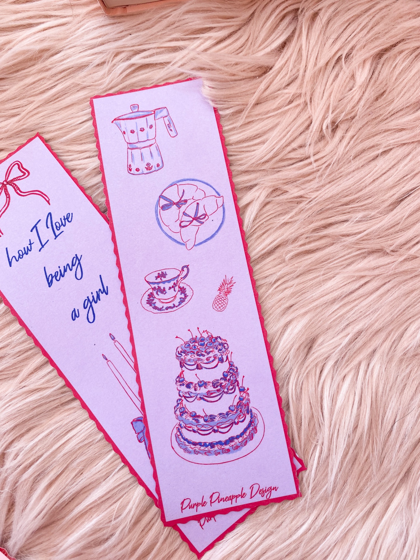 Marcador de livros branco com ilustrações em vermelho e azul, sobre pelúcia rosa