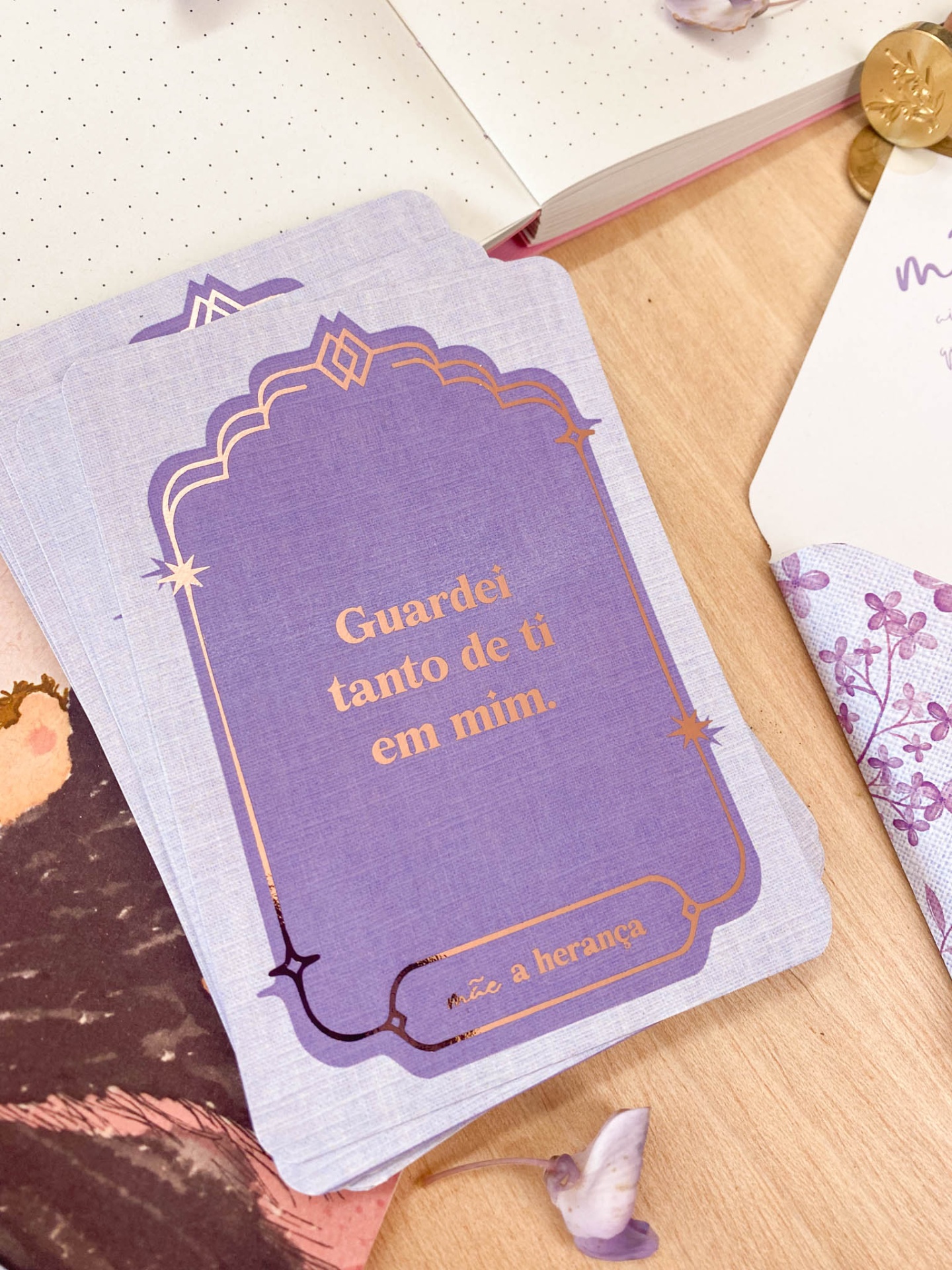 Cartas lilás com texto dourado numa mesa de madeira com elementos em papel e botões