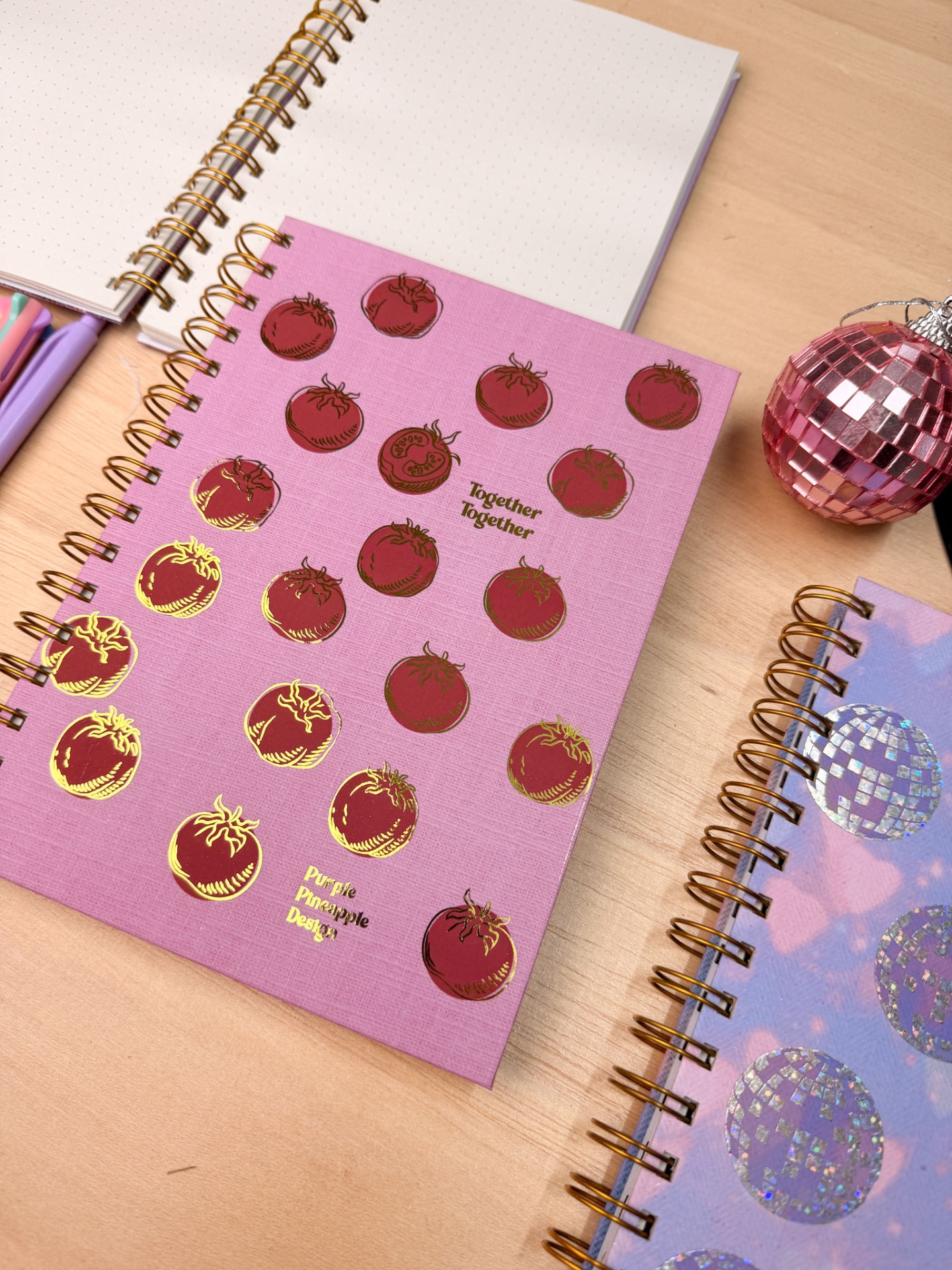Caderno rosa com desenhos de tomates e texto sobre mesa de madeira