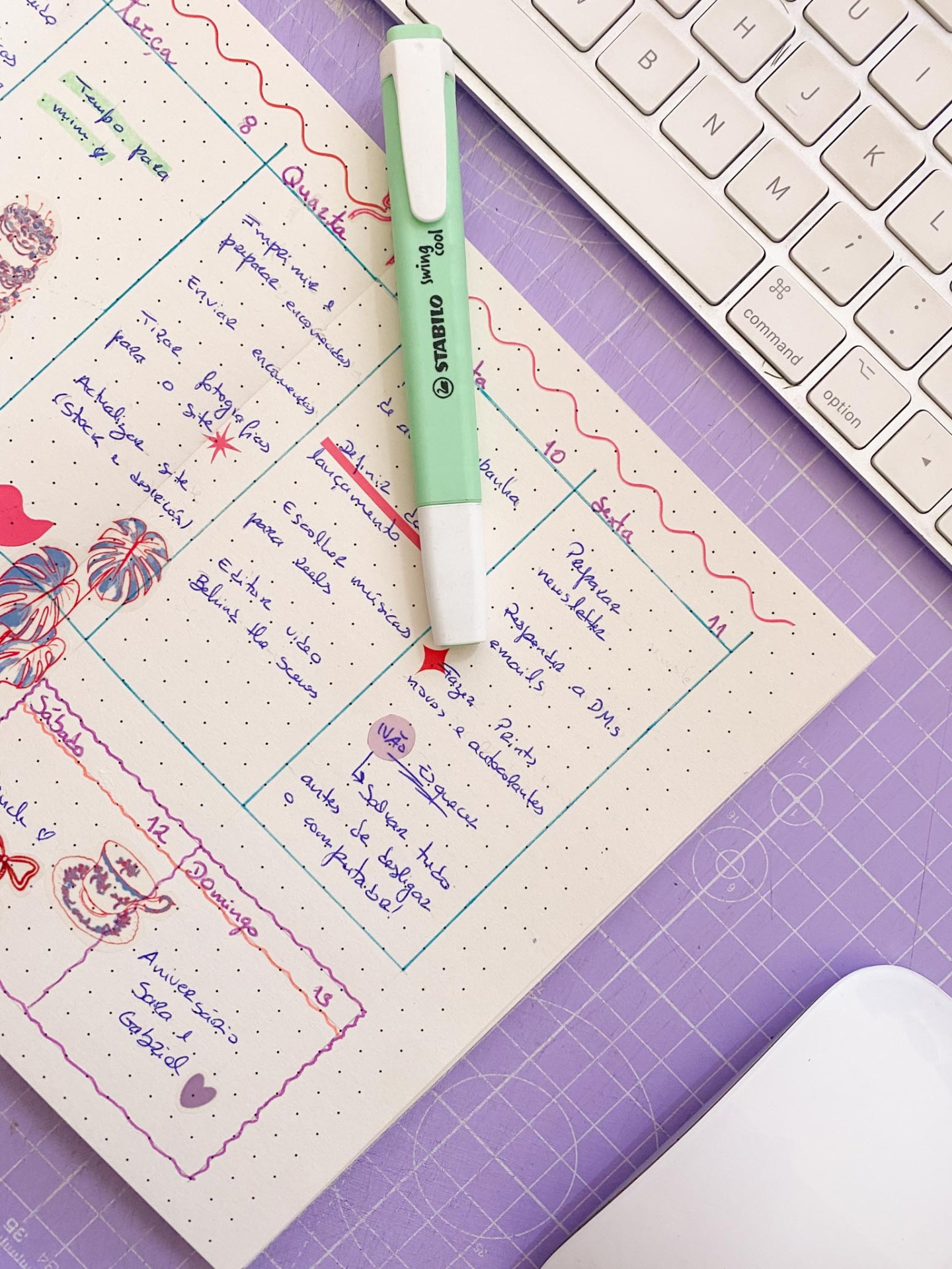Teclado branco, caneta Stabilo verde pastel e folha de planejador com escrita em português sobre mesa lilás