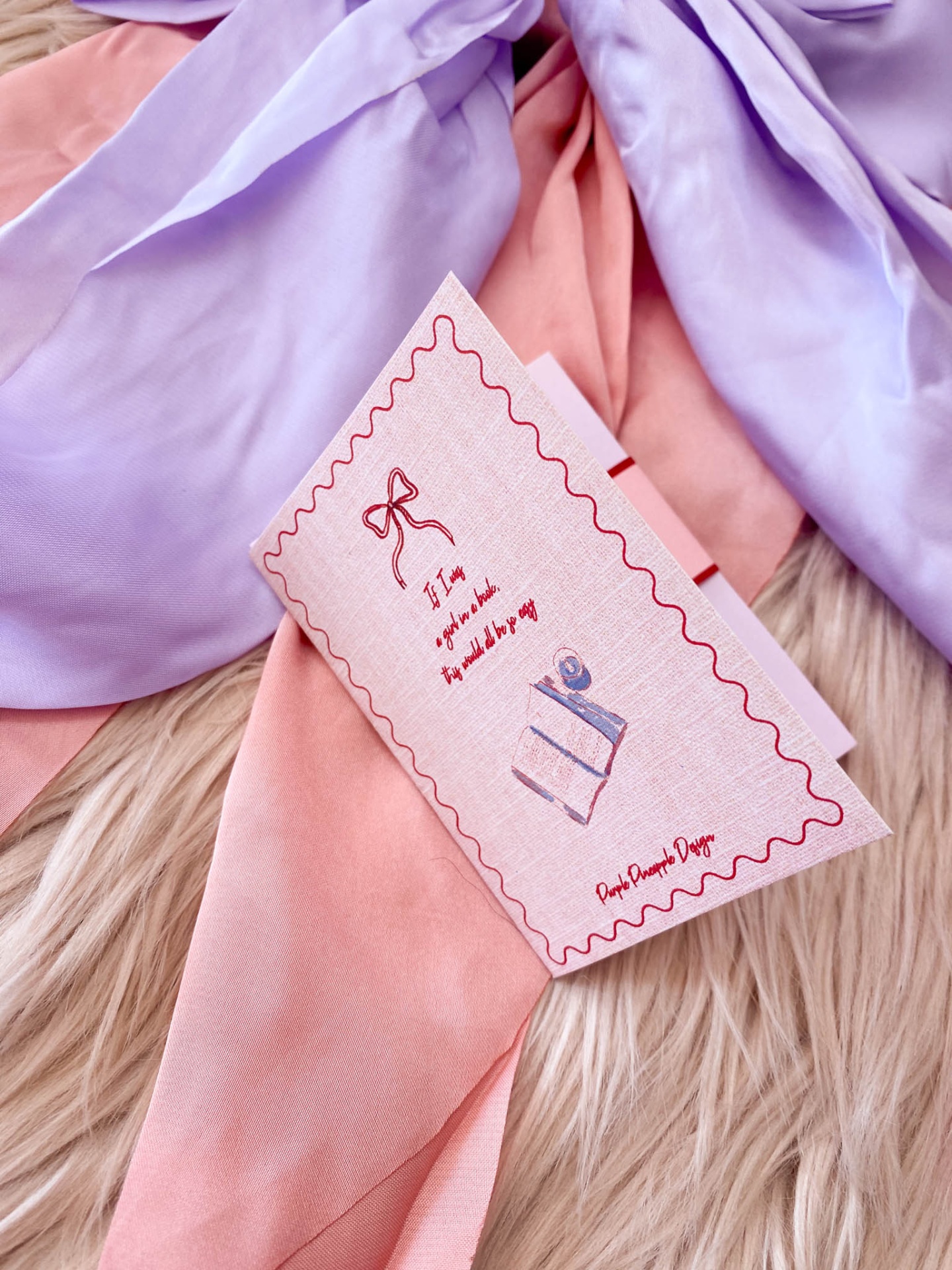 Lenços lilás e rosa com cartão rosa com desenho de livros e texto sobre superfície felpuda