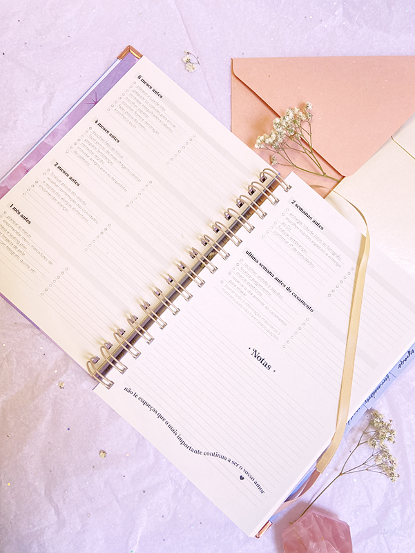 Agenda encadernada em espiral aberta com páginas para notas, fita marcadora e flores secas ao redor