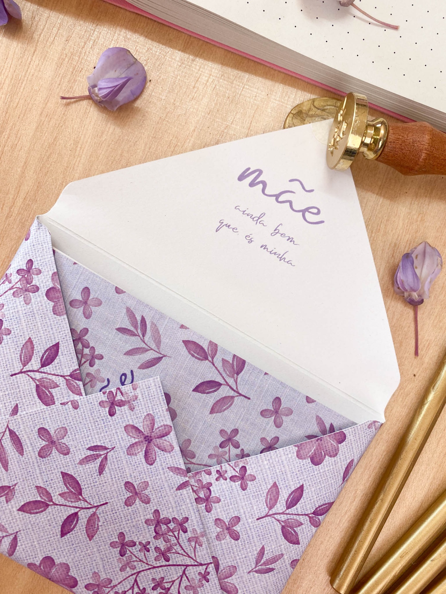 Envelope floral lilás aberto com texto para mãe, selo de cera e flores secas sobre madeira
