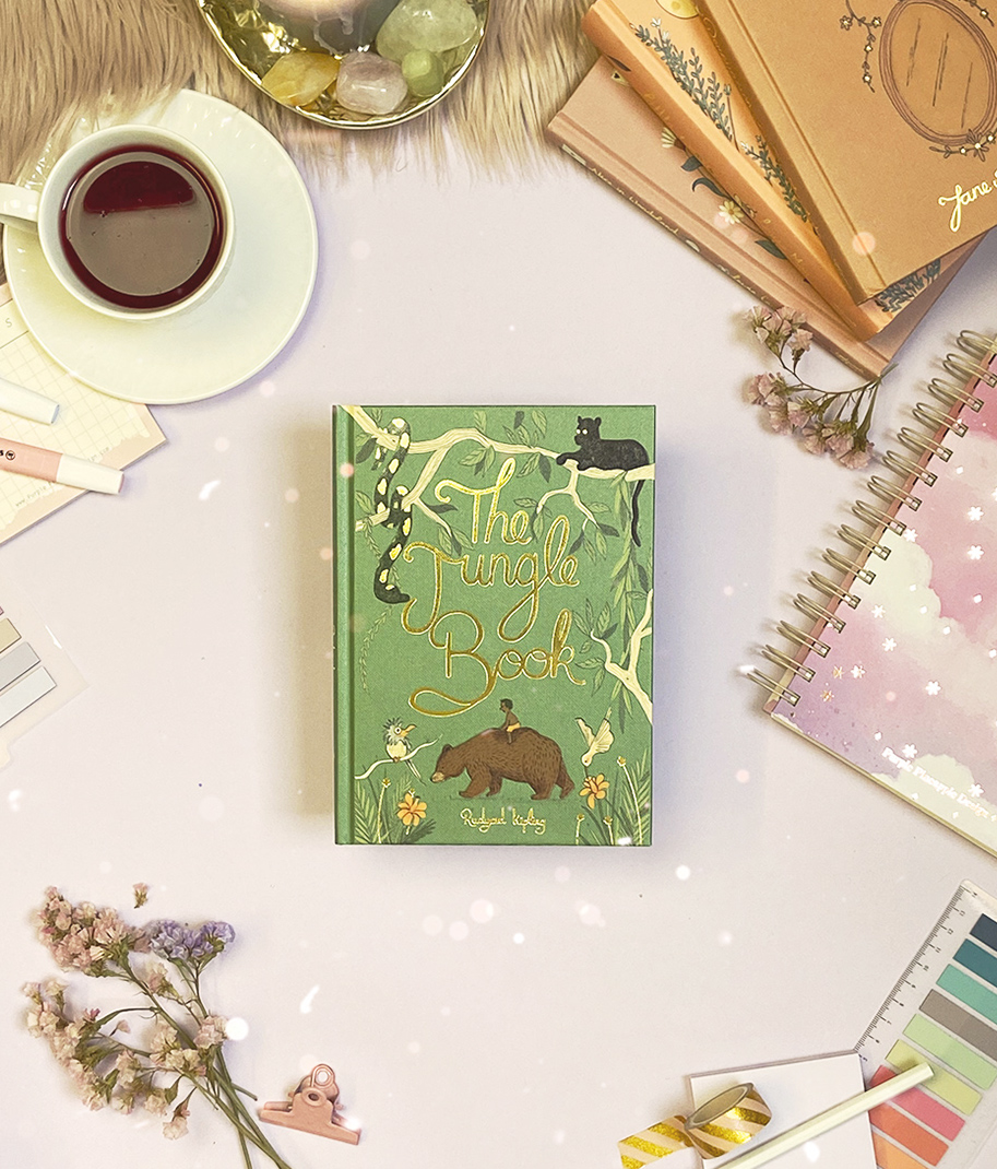 Livro The Jungle Book com capa verde ilustrada, rodeado por material de escritório e flores numa mesa clara.