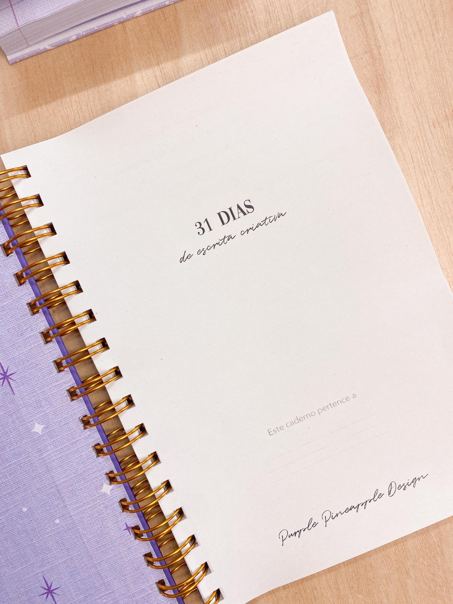 Caderno espiral branco com texto, tecido lilás com estrelas ao lado