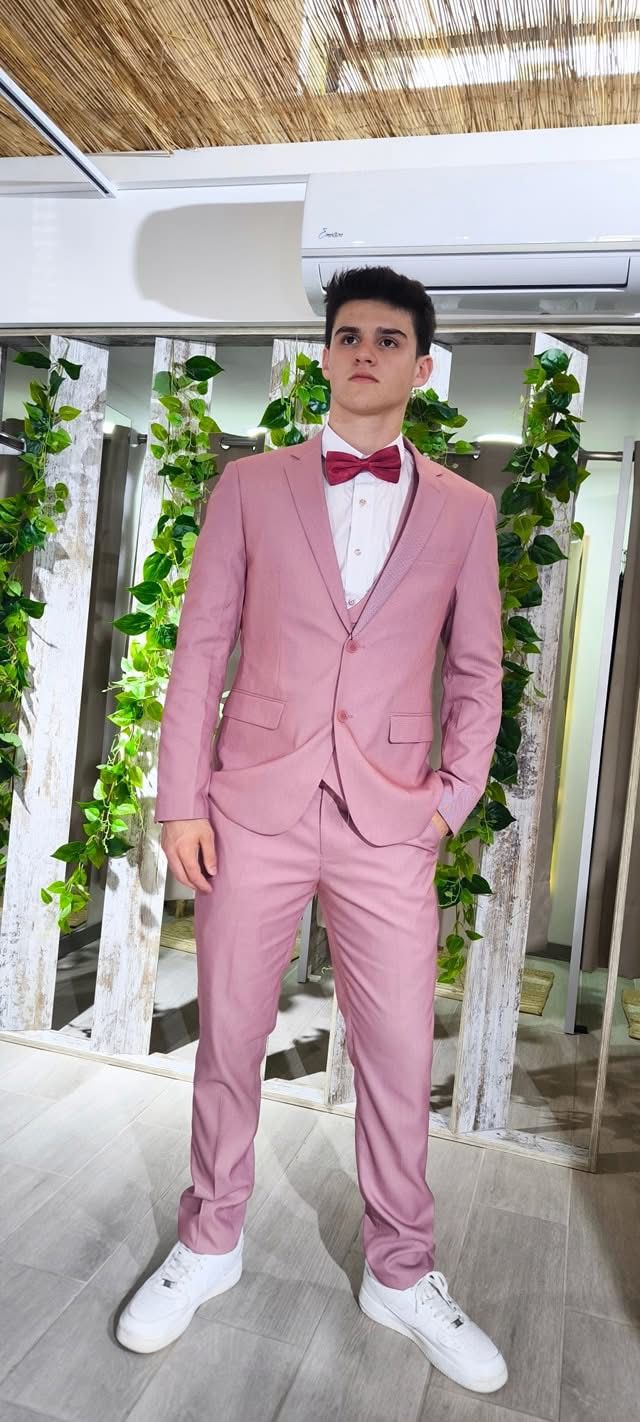 Fato Rosa Ponteado Homem de fato rosa claro com gravata borboleta vermelha em ambiente interior com plantas.