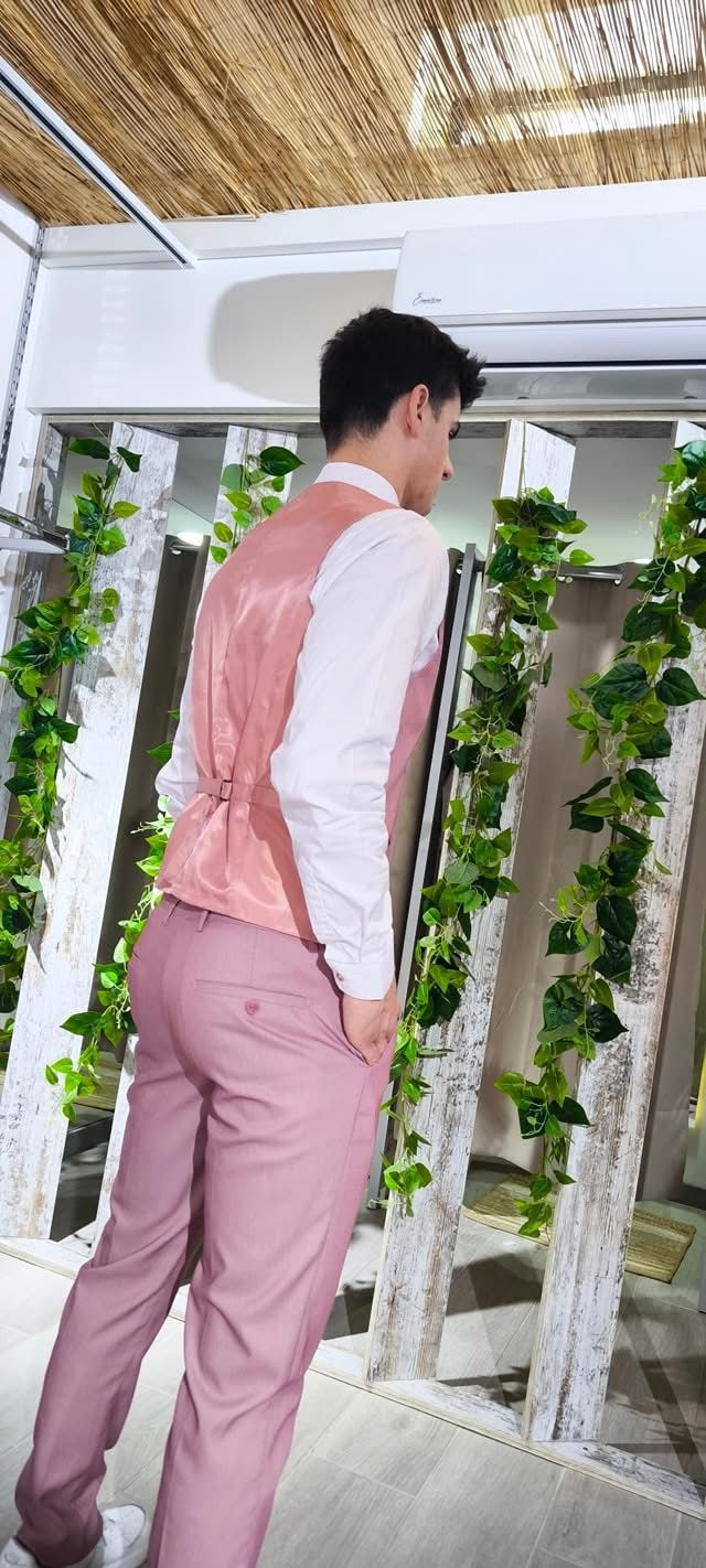 Fato Rosa Ponteado Homem a usar colete rosa e calças cor-de-rosa em ambiente com decoração de plantas e teto de palha