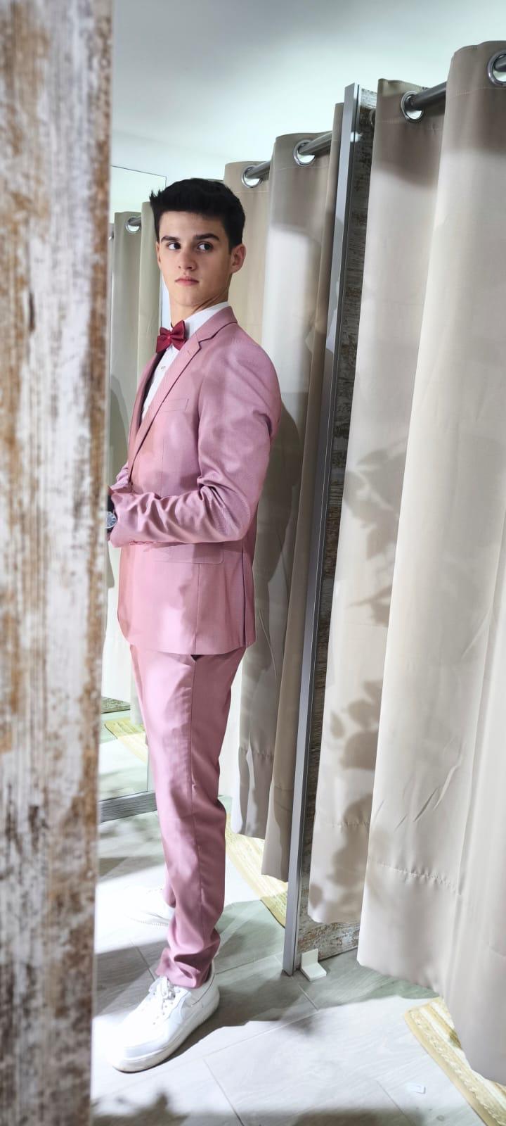 Fato Rosa Ponteado Jovem com fato rosa e gravata borboleta posando junto a cortinas bege