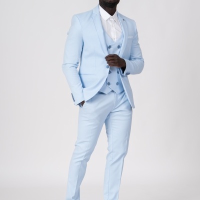 Homem com fato azul claro, camisa branca e sapatos escuros em fundo branco.