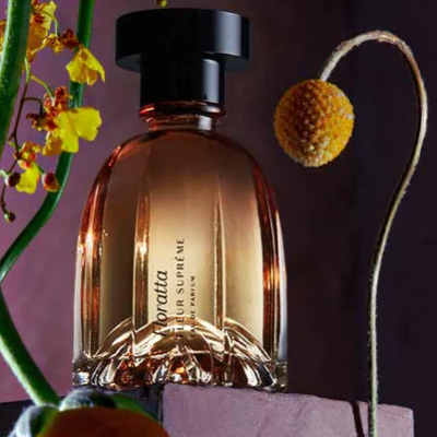 Frasco de perfume âmbar com tampa preta e flores amarelas e castanhas ao redor