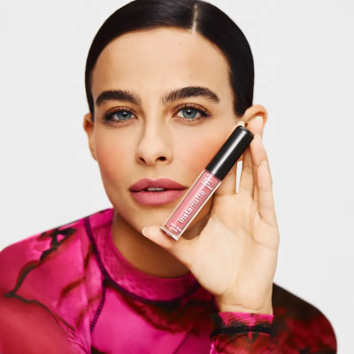 Mulher segura batom líquido rosa com tampa preta e texto Instamate Lip
