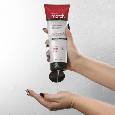 Tubo de produto Match Science Reconstrução com mãos femininas e gotas de água ao fundo.