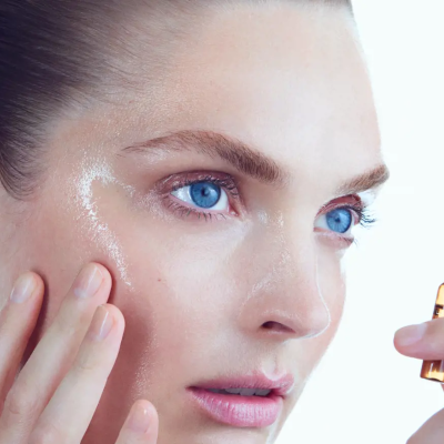 Rosto feminino com pele luminosa segurando ampola âmbar pequena