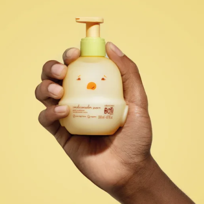 Frasco amarelo claro com dispenser laranja e rosto de pássaro segurado por uma mão