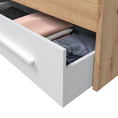 Cajão branco aberto com roupa dobrada dentro num móvel de madeira clara