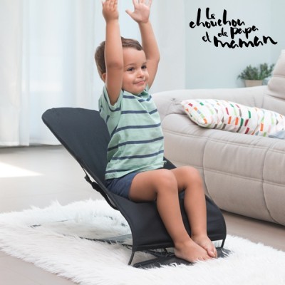 Cadeira de bebé preta com criança sentada, sala clara com sofá e tapete branco