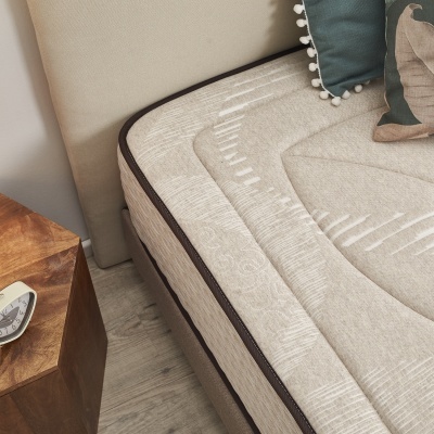 Colchão bege com padrões em relevo e borda escura perto de cabeceira e mesa de madeira