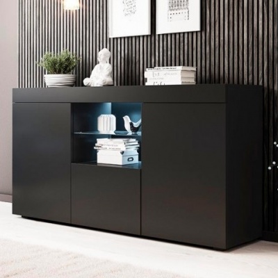 Aparador preto com prateleira de vidro e iluminação, decorado com objetos e livros, contra parede preta geométrica.