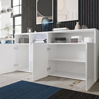 Móvel branco de sala com duas portas abertas e prateleiras, sobre tapete azul e preto e parede preta canelada ao fundo