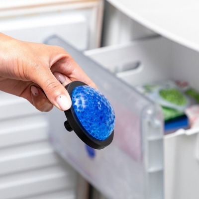 Mão a segurar objeto redondo azul com base preta junto a congelador aberto