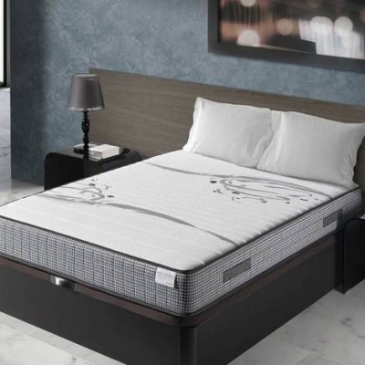 Colchão branco com padrão cinza e detalhes florais numa cama com cabeceira de madeira e mesa de cabeceira preta