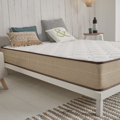 Colchão bege em cama branca com almofadas e tapete geométrico