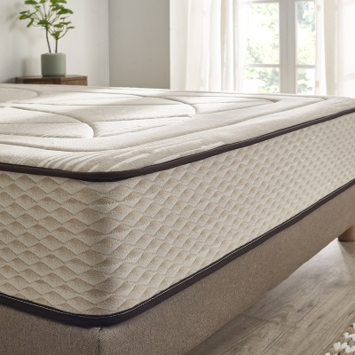 Colchão bege com padrão geométrico acolchoado sobre estrutura de cama em tecido bege num quarto iluminado.