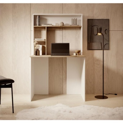 Secretária em madeira clara com computador e estantes, lâmpada de pé preta e tapete branco
