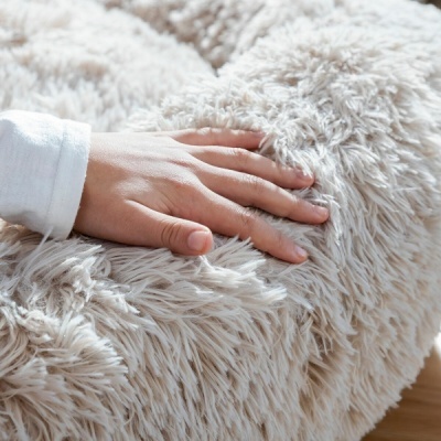 Mão sobre almofada felpuda bege claro em chão de madeira