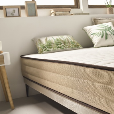 Colchão bege anatómico com bordas castanhas e almofadas com estampado de folhas verdes