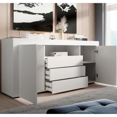 Móvel branco com gavetas e portas abertas, decorado com livros, vaso com flores secas e quadros em preto e branco