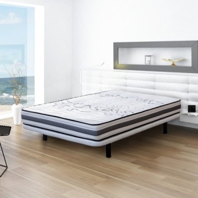 Cama com colchão branco e cinzento numa sala luminosa com vista para o mar