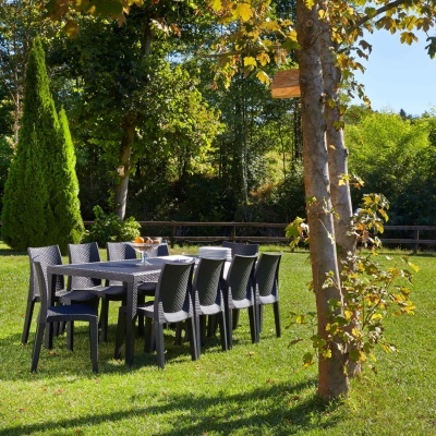 Conjunto de mesa e cadeiras pretas em plástico estilo rattan num jardim com relvado e árvores.